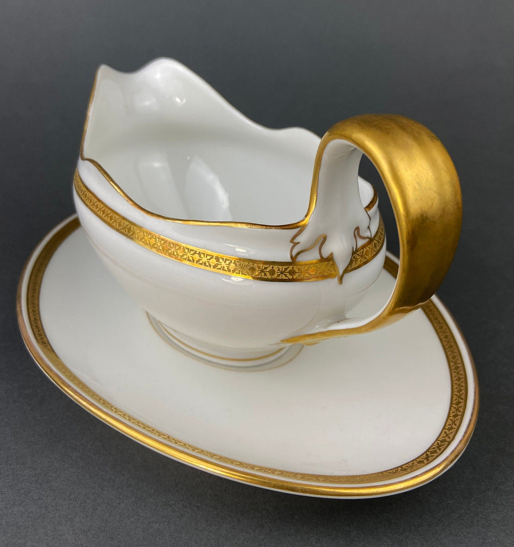 White porcelain soup boat with gold handle, gold rim band, and crest decoration