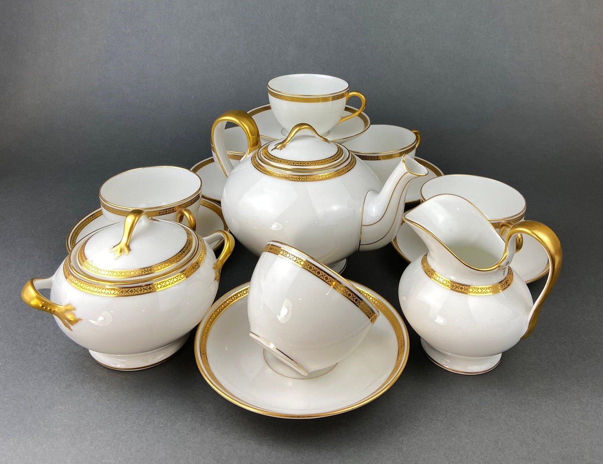 White porcelain tea and serving set with gold handles, lids, saucers, and tray