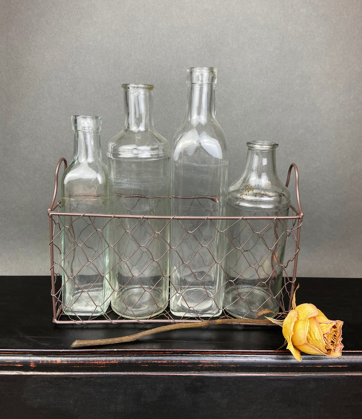 Clear glass bottles in rose-gold wire basket with small yellow rose accents