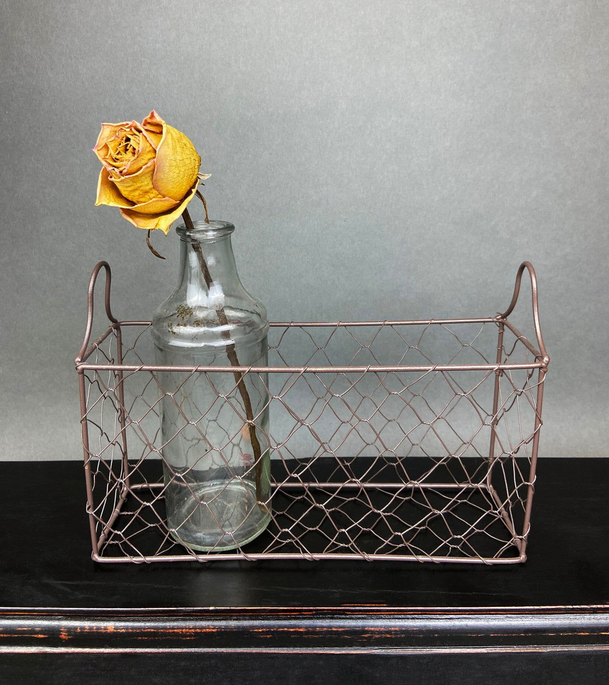 Clear glass bottle in rose-gold metal basket with a yellow rose flower