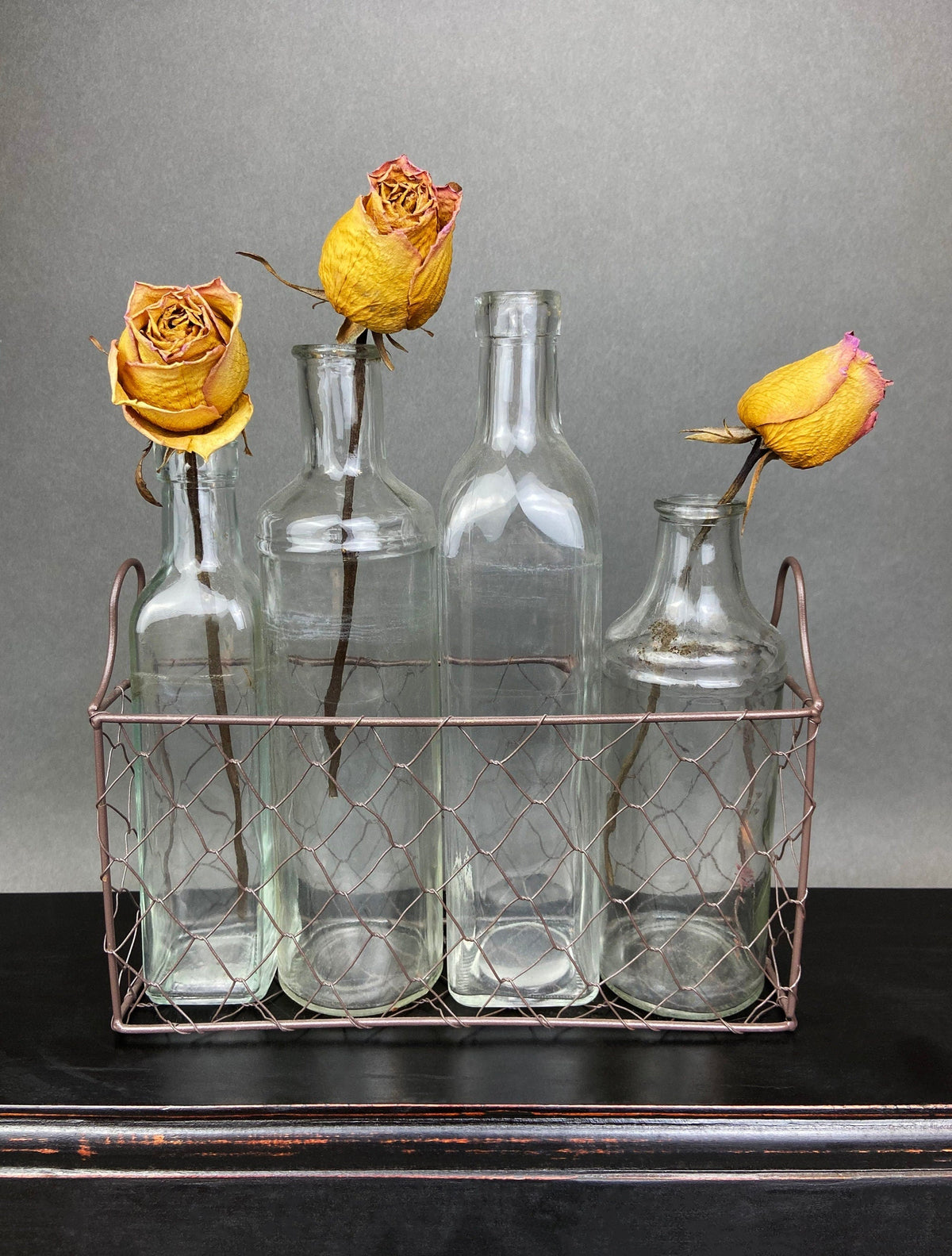 Clear glass apothecary bottles with rose-gold metal basket and yellow rose flowers