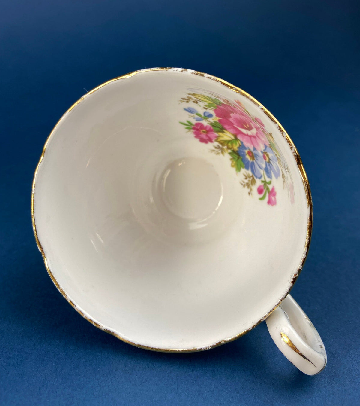 White teacup interior with floral bouquet and gold rim; handle on right