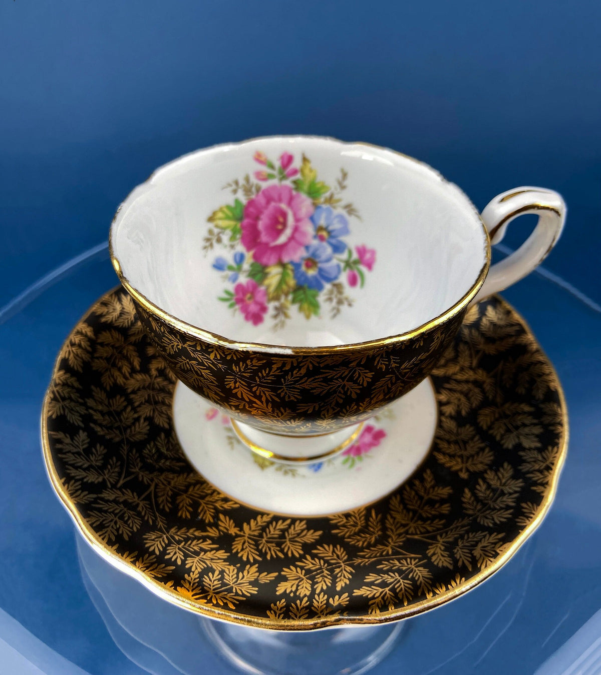 Black teacup and matching saucer with gold trim and colorful floral bouquet design