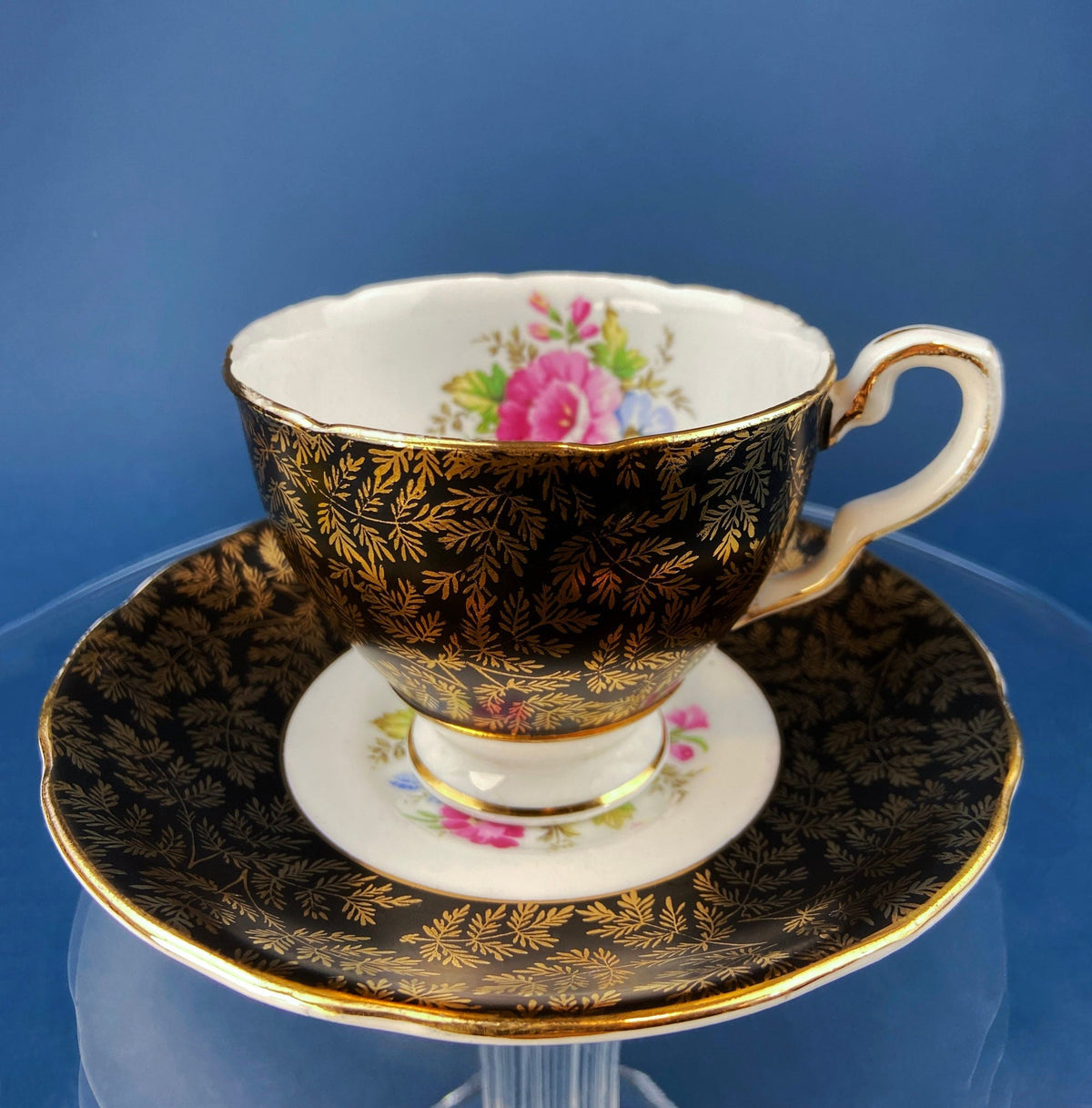 Black porcelain cup and saucer set with gold leafy border and pink floral bouquet
