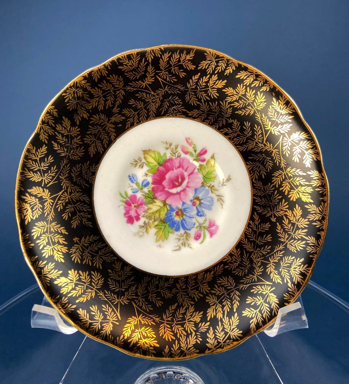 Black porcelain saucer with gold leafy pattern border and central pink floral bouquet