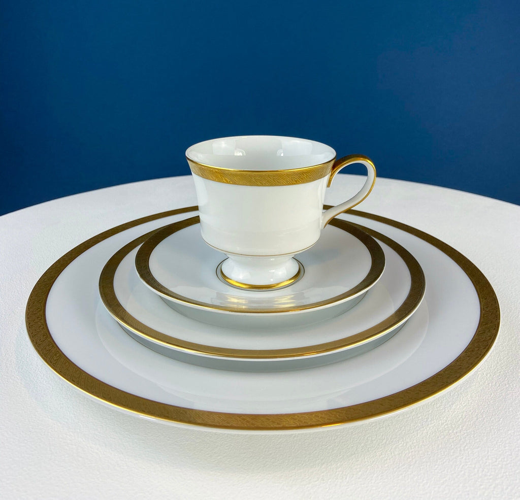 White porcelain teacup with gold band on stacked saucers and plate