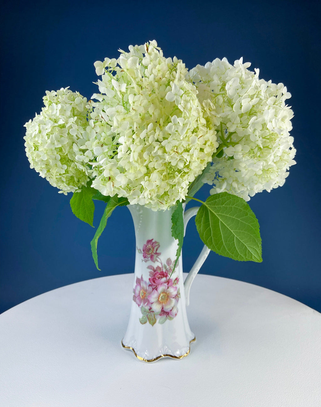 White porcelain vase with green hydrangea-like blooms and small floral accents