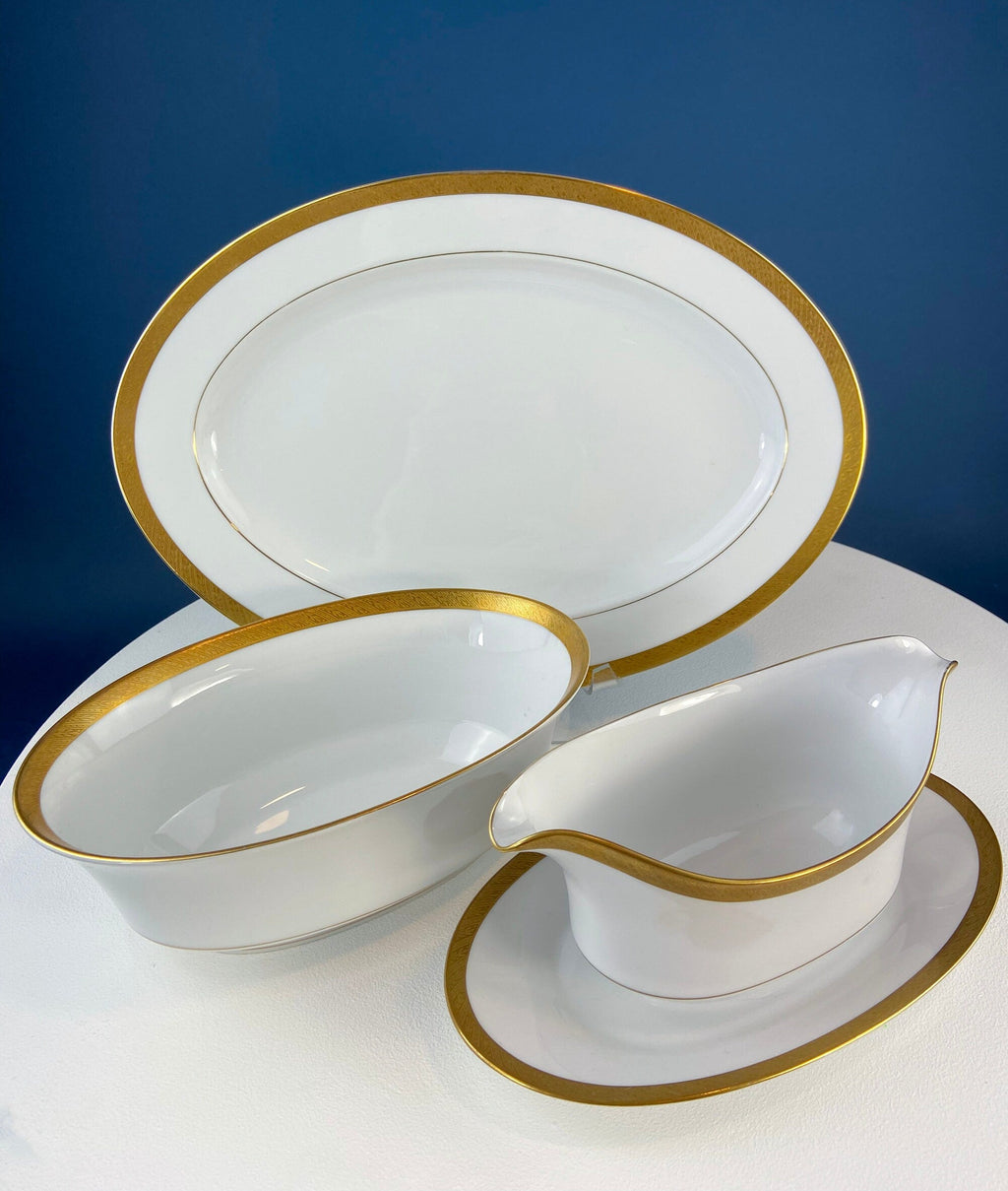 White porcelain serving pieces with gold rims, including an oval platter