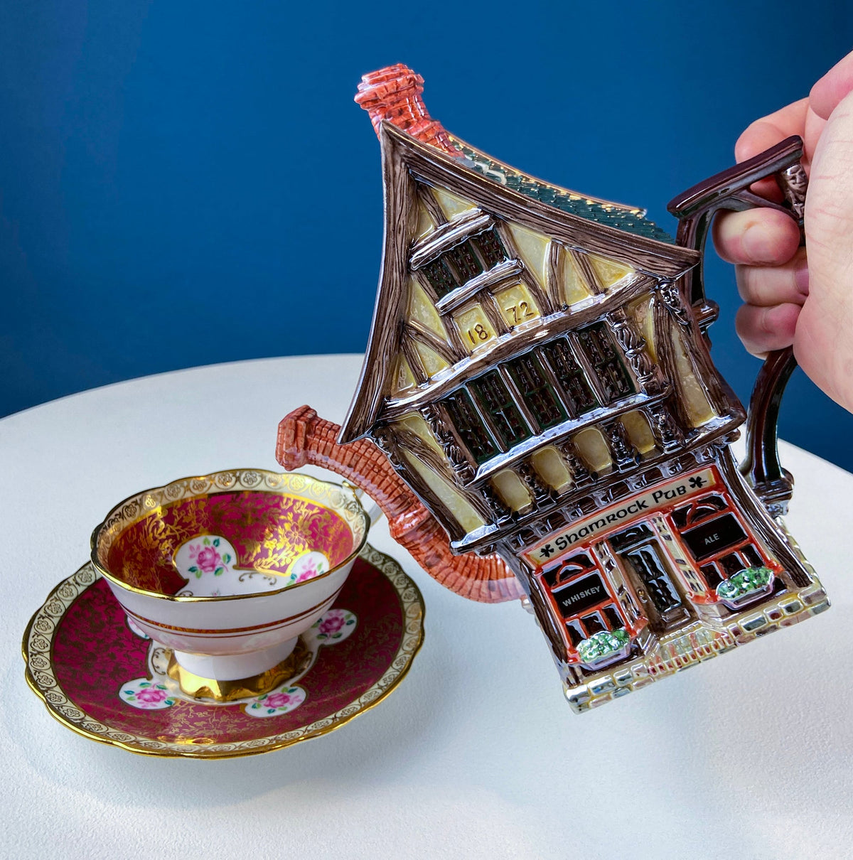 House-shaped ceramic pub display with cup and saucer, hand holding handle