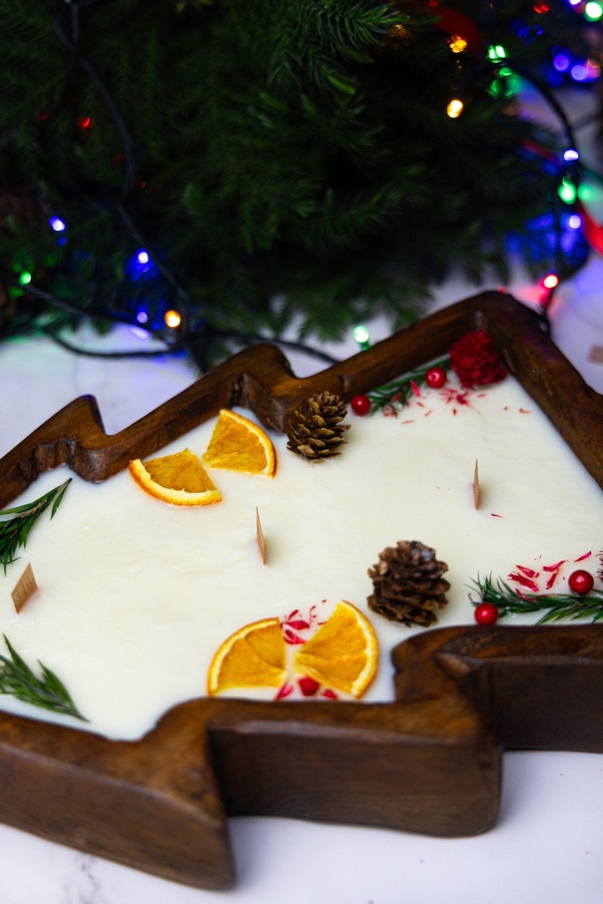 Christmas tree wooden dough bowl candle with white wax, citrus slices, pinecones, and red berries