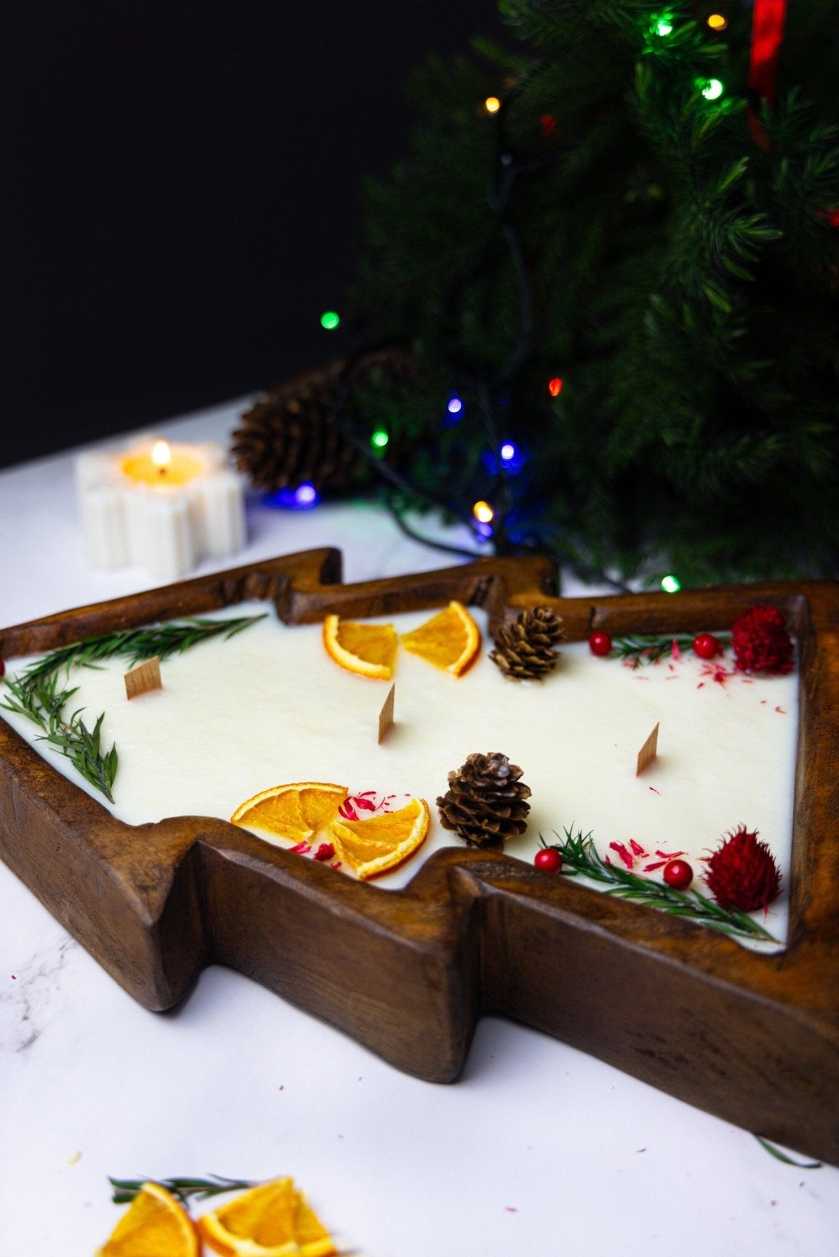 Christmas tree-shaped wooden dough bowl candle with white wax, citrus slices, pinecones, and herbs