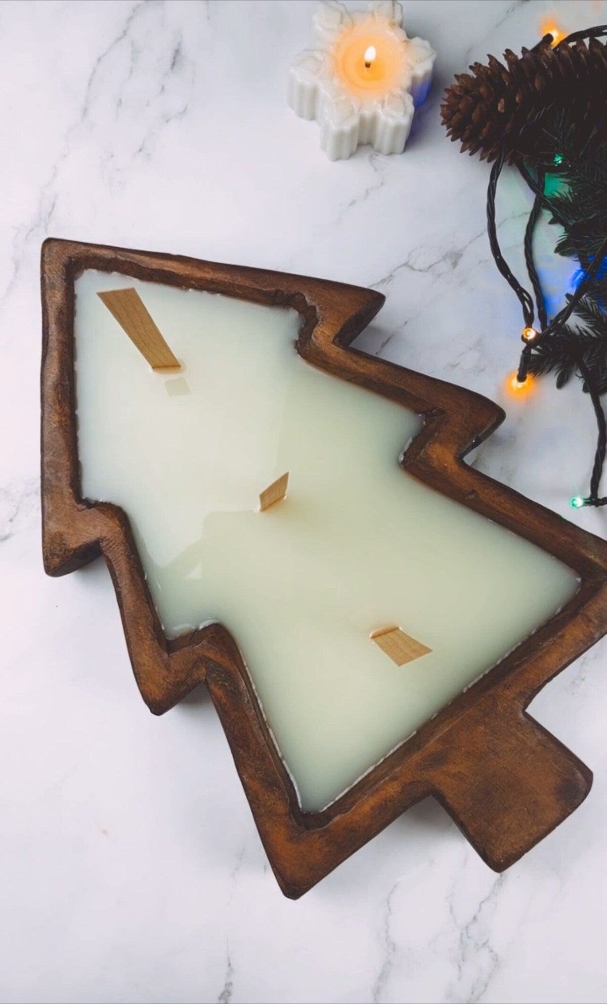 Christmas tree-shaped wooden dough bowl candle with white wax and small embedded wood pieces