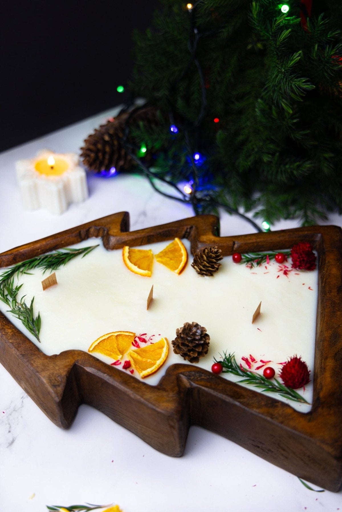 Christmas tree-shaped wooden dough bowl candle with white wax, citrus slices, and pine accents