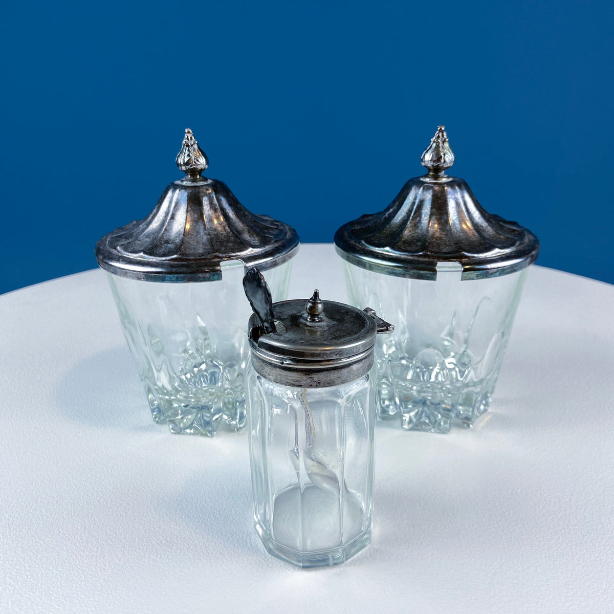 Three clear glass jars with decorative silver lids and finials, relish or jam set