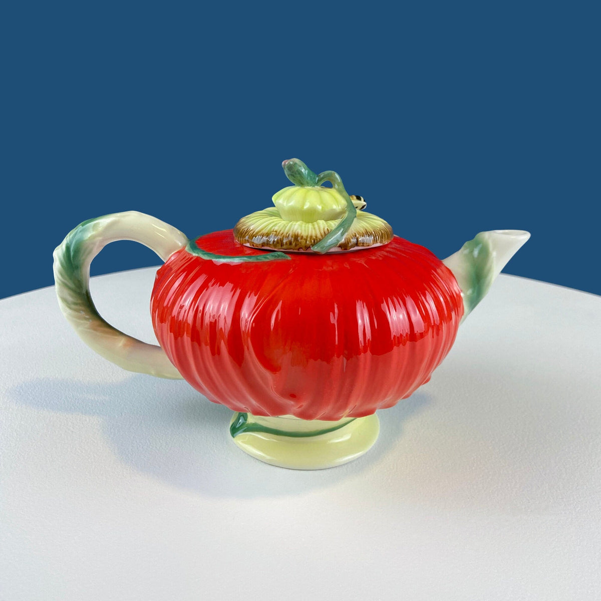 Red poppy-shaped ceramic teapot with curved spout, two handles, and bee lid