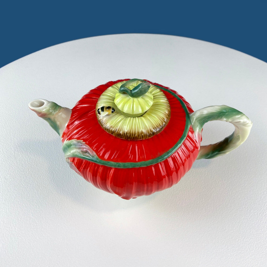 Red poppy-shaped teapot with green-trim lid and yellow bee ornament on top