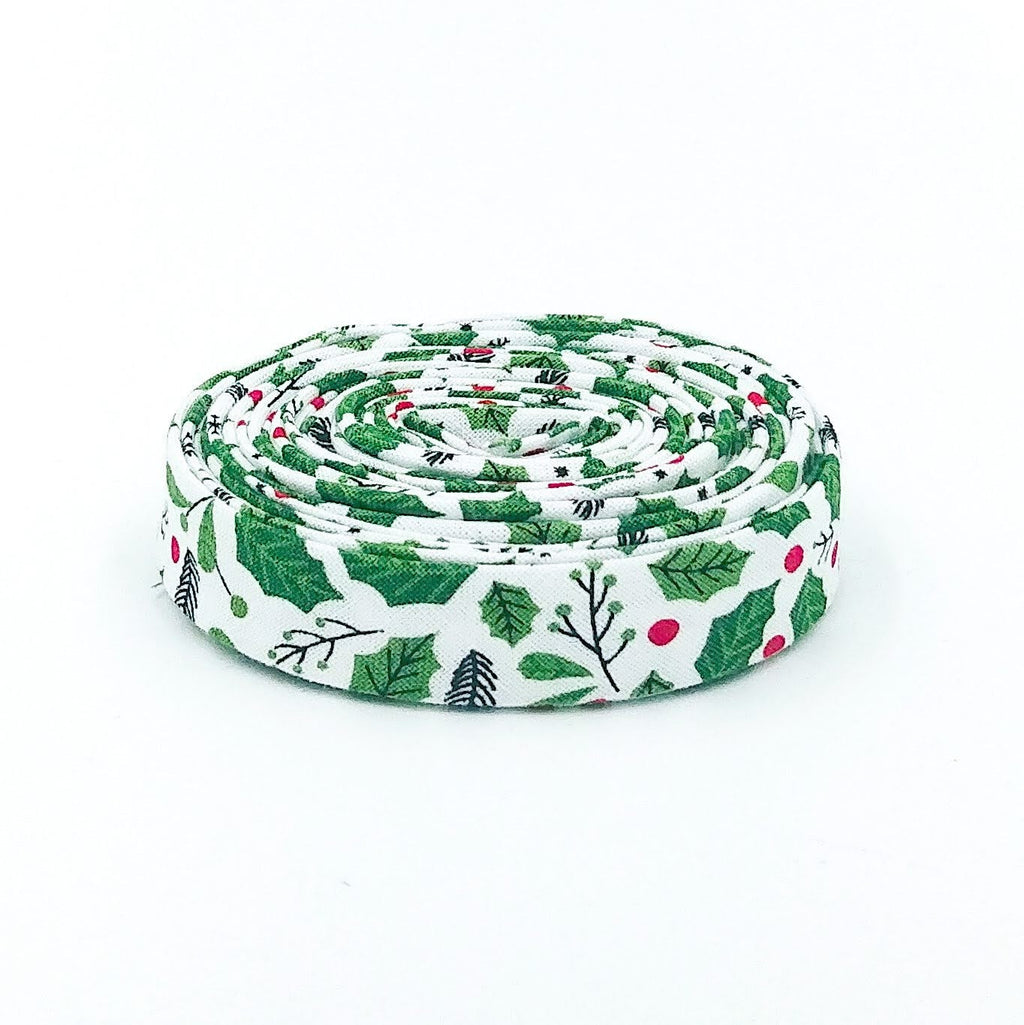 Double-fold 1/2in bias tape in white, green holly and red berry print, tightly coiled roll