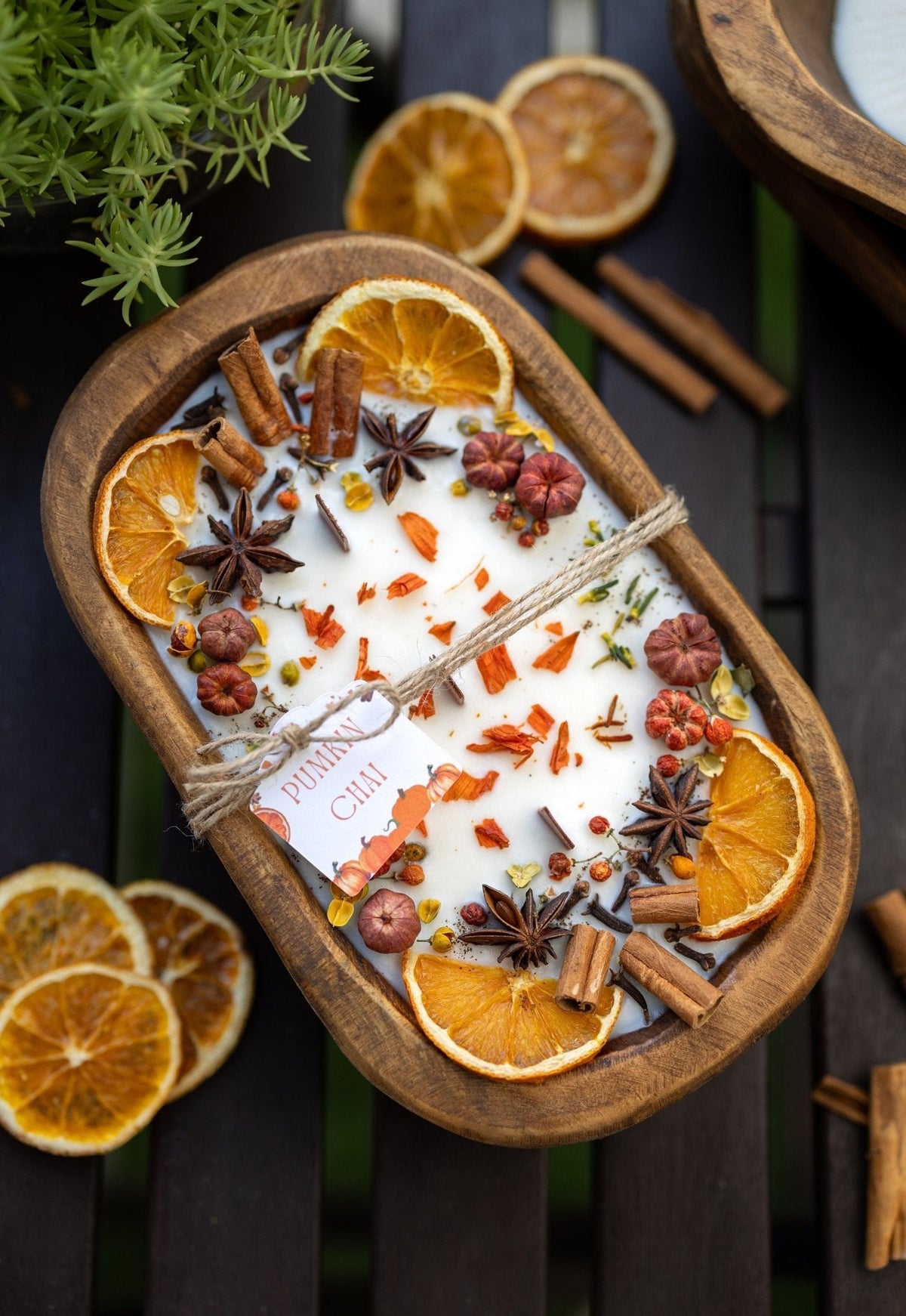 Decorative autumn candle in wooden bowl with orange slices, cinnamon sticks, and star anise