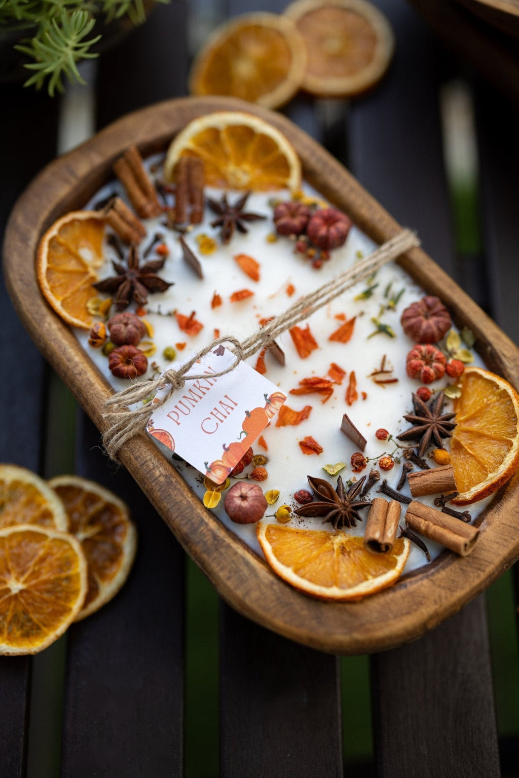 Decorative autumn candle in wooden bowl with orange rounds, dried berries, and spice sprinkles