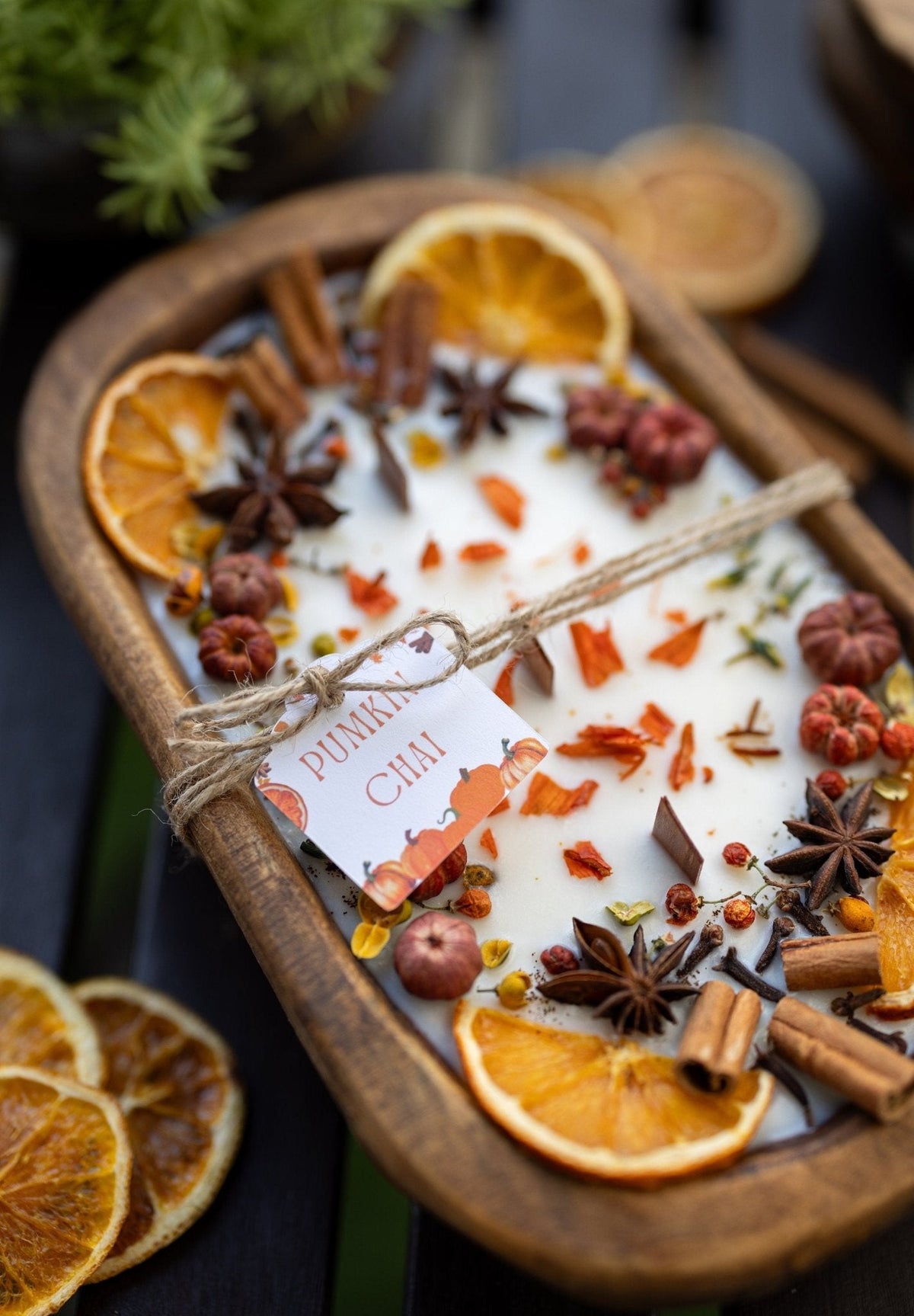 Decorative autumn candle in wooden bowl with orange slices and spices; close-up angle