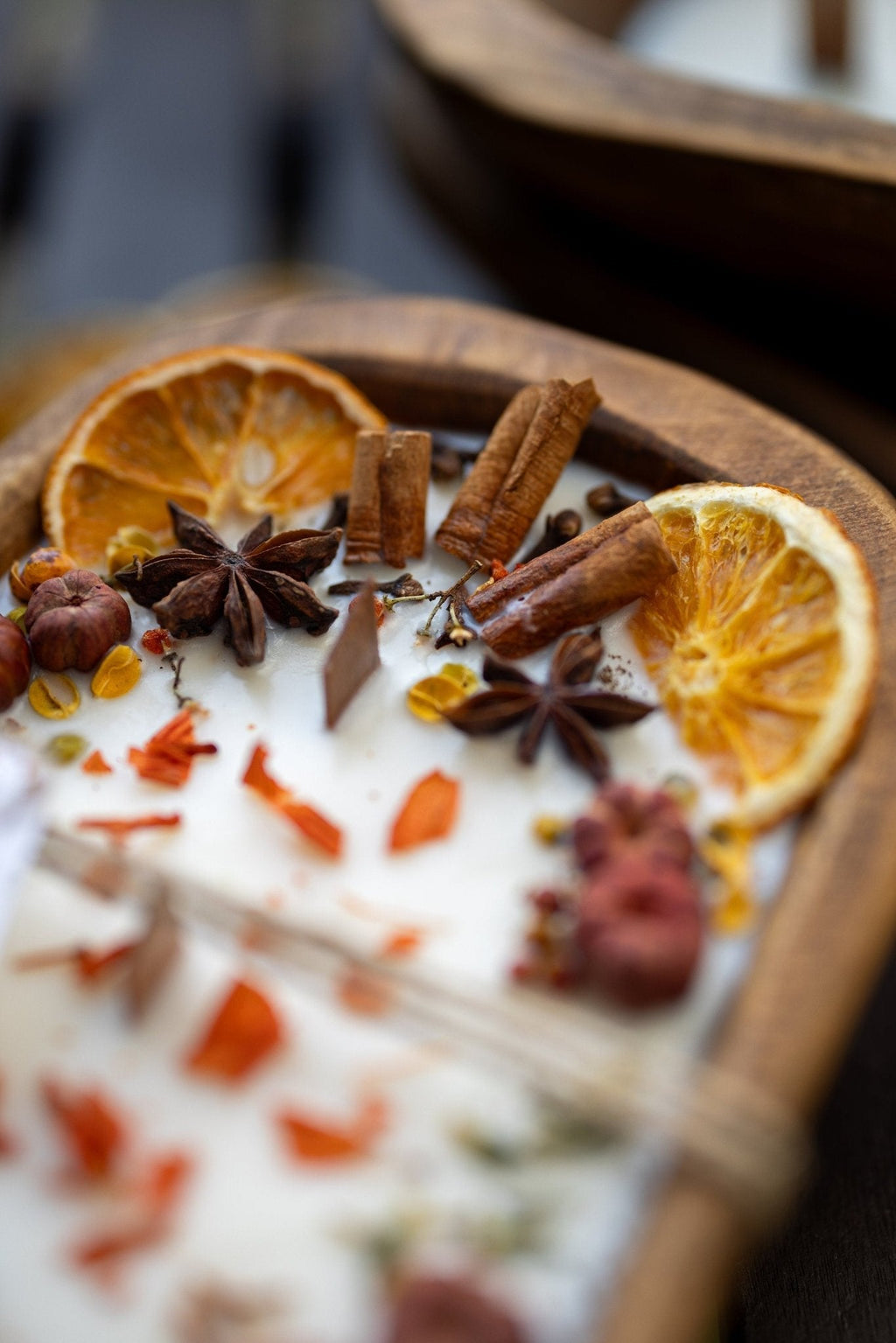 Decorative autumn candle in wooden bowl with orange slices, cinnamon sticks, and star anise