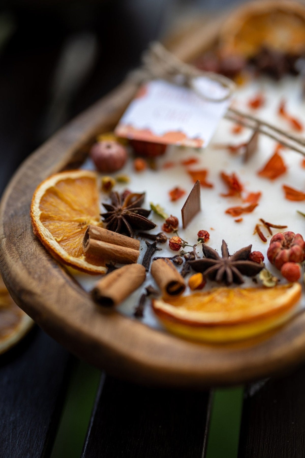 Decorative autumn candle in wooden bowl on stand; orange slices and cinnamon stick detail