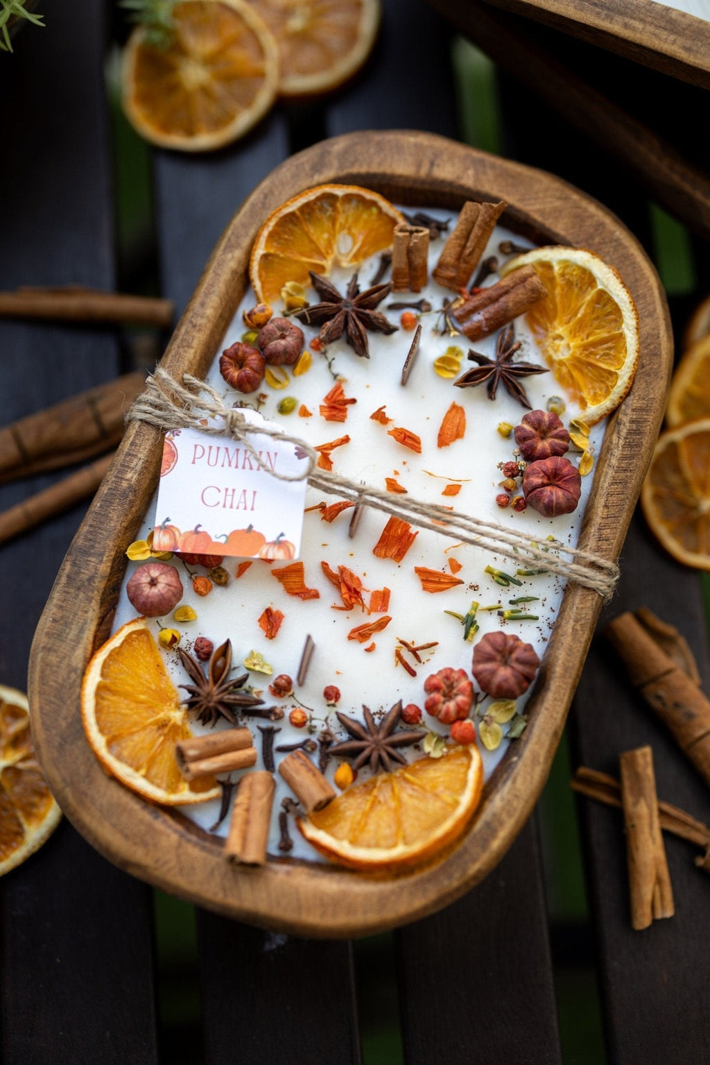 Decorative autumn candle in wooden bowl with orange rounds, star anise, and spice mix