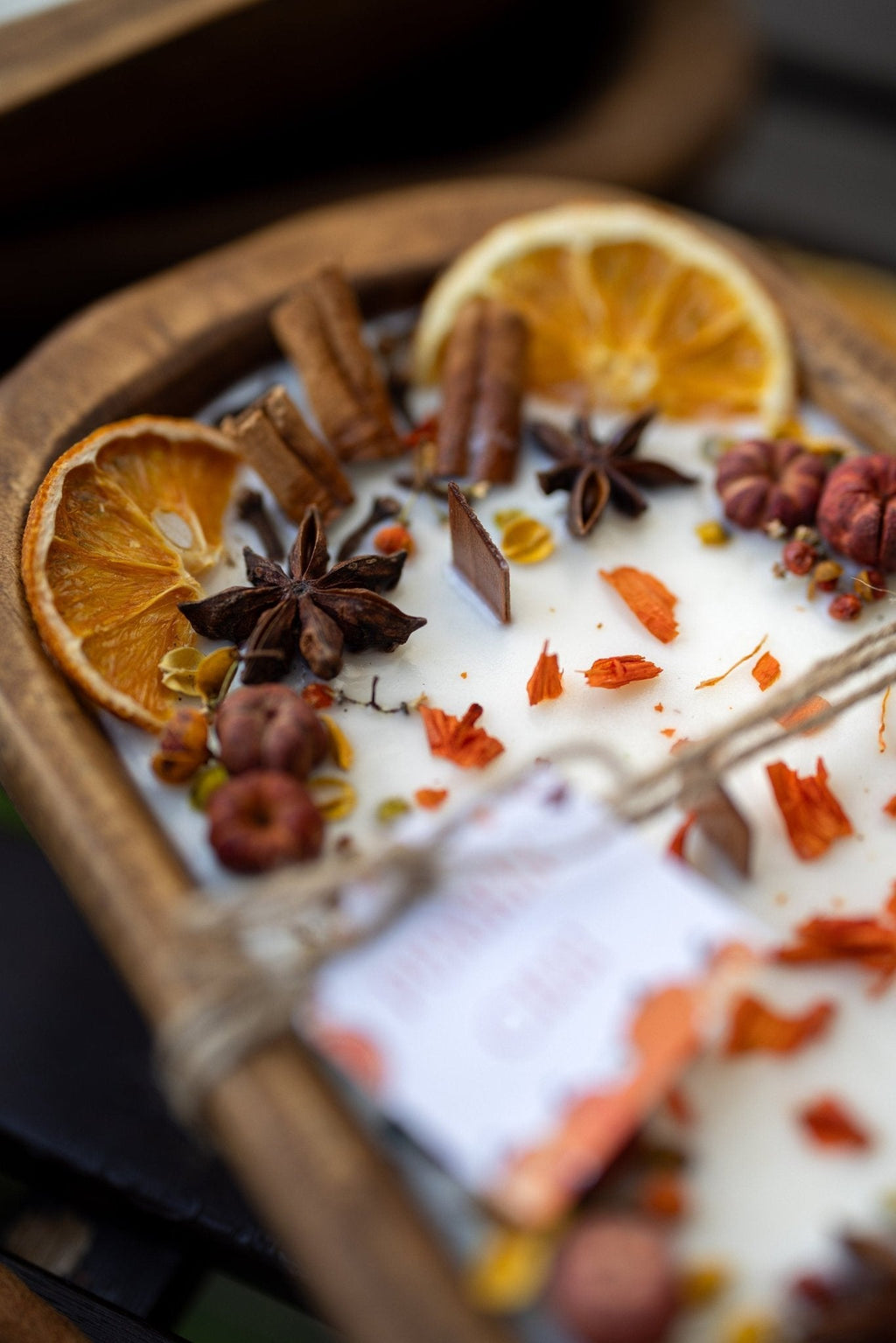 Decorative autumn candle in wooden bowl with orange slices and star anise; blurred background