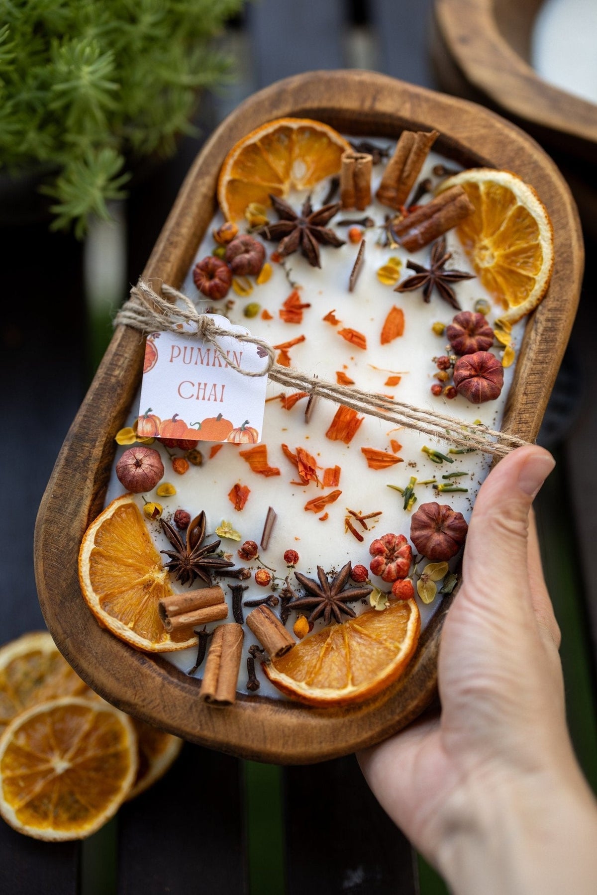 Decorative autumn candle in wooden bowl held by hand; orange slices and cinnamon sticks