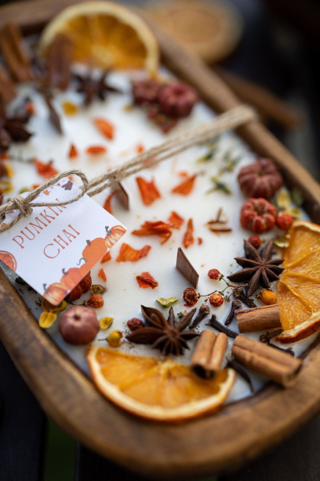 Decorative autumn candle in wooden bowl with orange slices, star anise, and spice mix