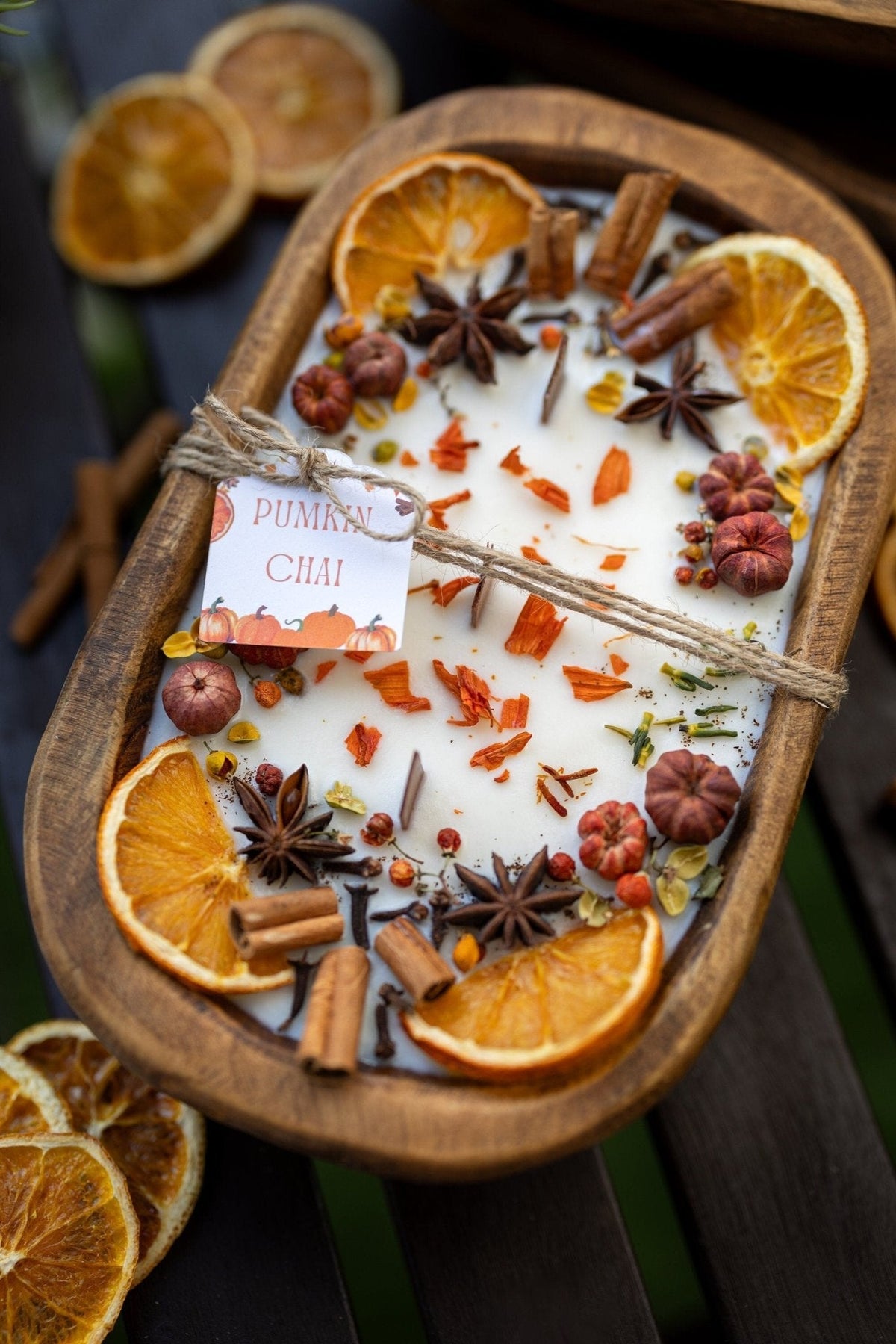 Decorative autumn candle in wooden bowl with orange slices, cinnamon sticks, and spices