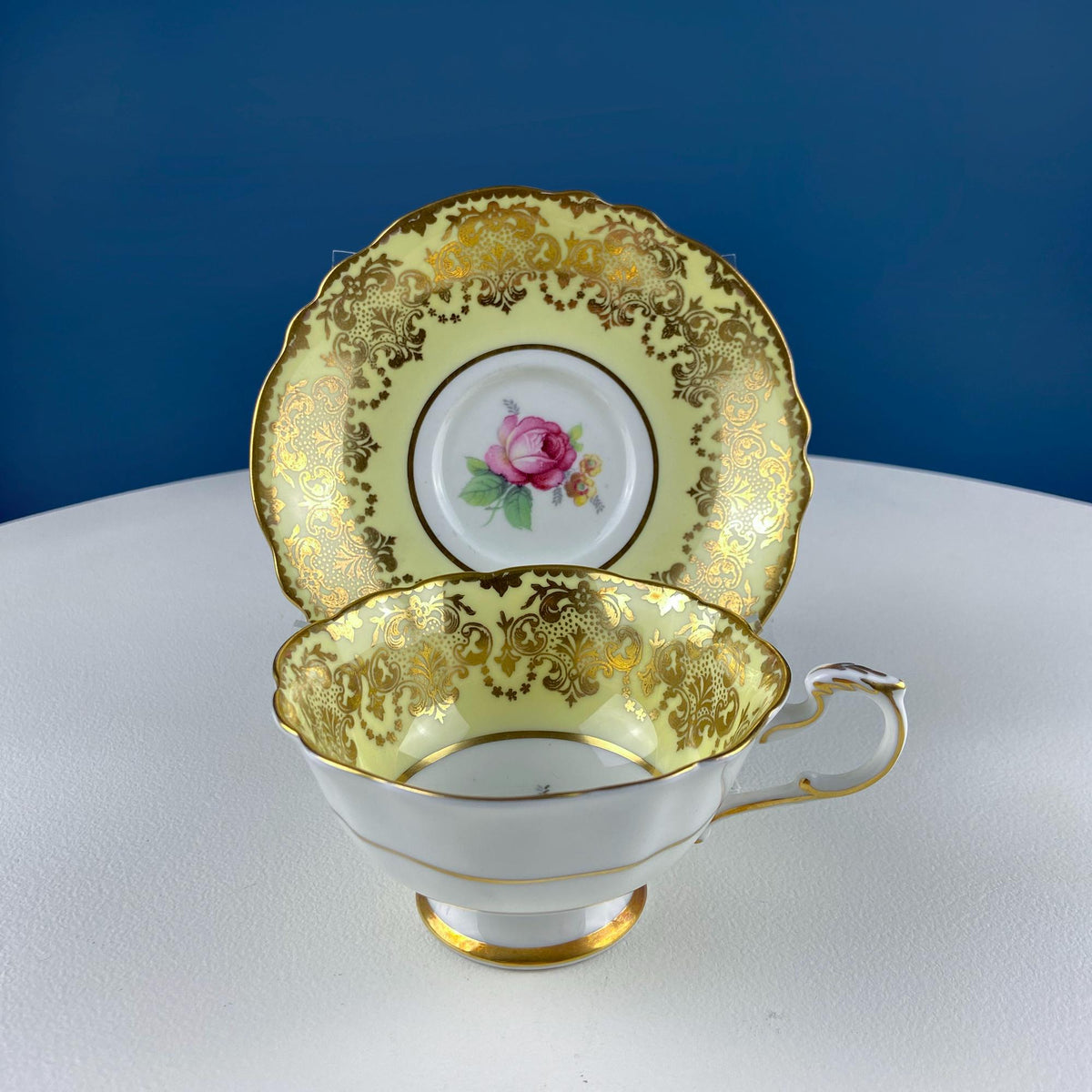 Vintage tea cup and saucer set with gold scrolling trim and pink rose inside medallion