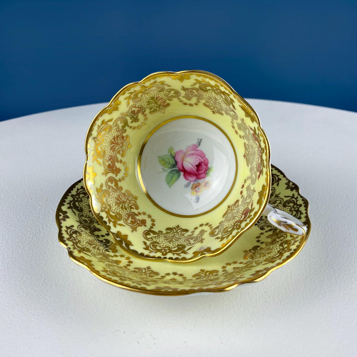 Yellow tea cup on matching saucer with gold filigree rim and pink rose medallion