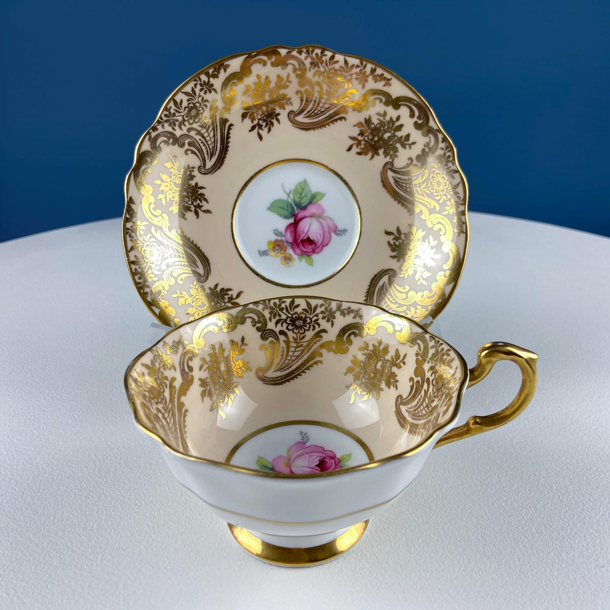 Stacked tea cup and saucer with pink rose center, gold scrollwork trim, curved handle
