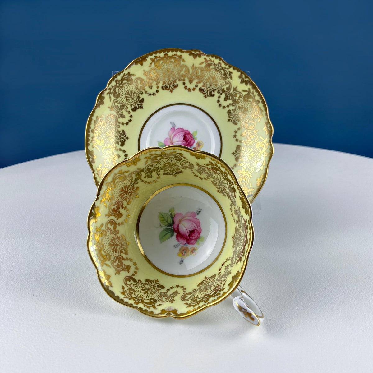 Yellow tea cup and saucer set with gold floral border and pink rose center, curved handle