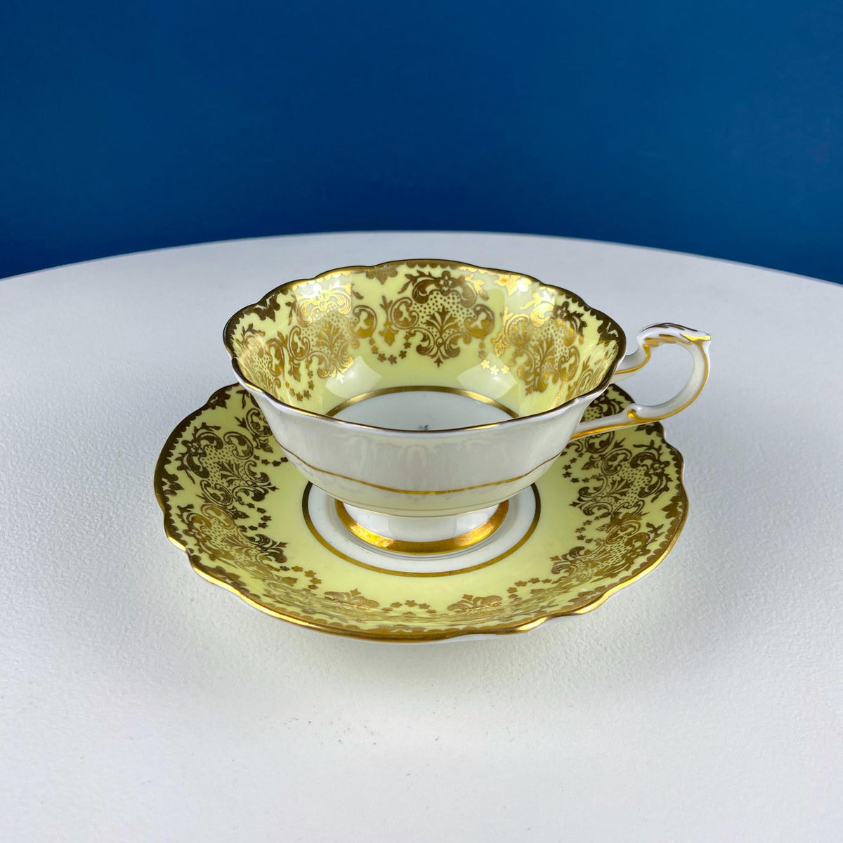 Yellow tea cup with side handle and gold trim on patterned saucer, pink rose center