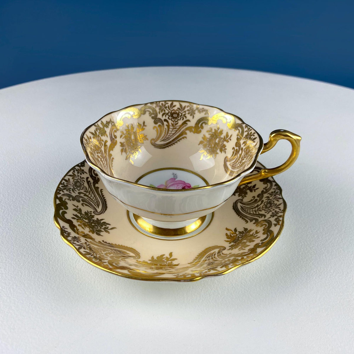 Tea cup on matching saucer with pink rose medallion and gold trim, side view