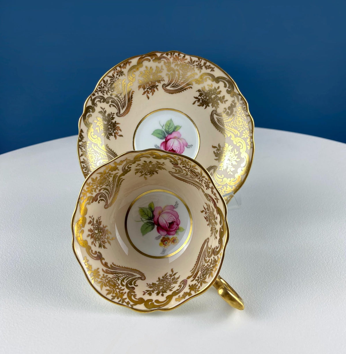 Tea cup and saucer set with pink rose motif, ornate gold border, scalloped rims
