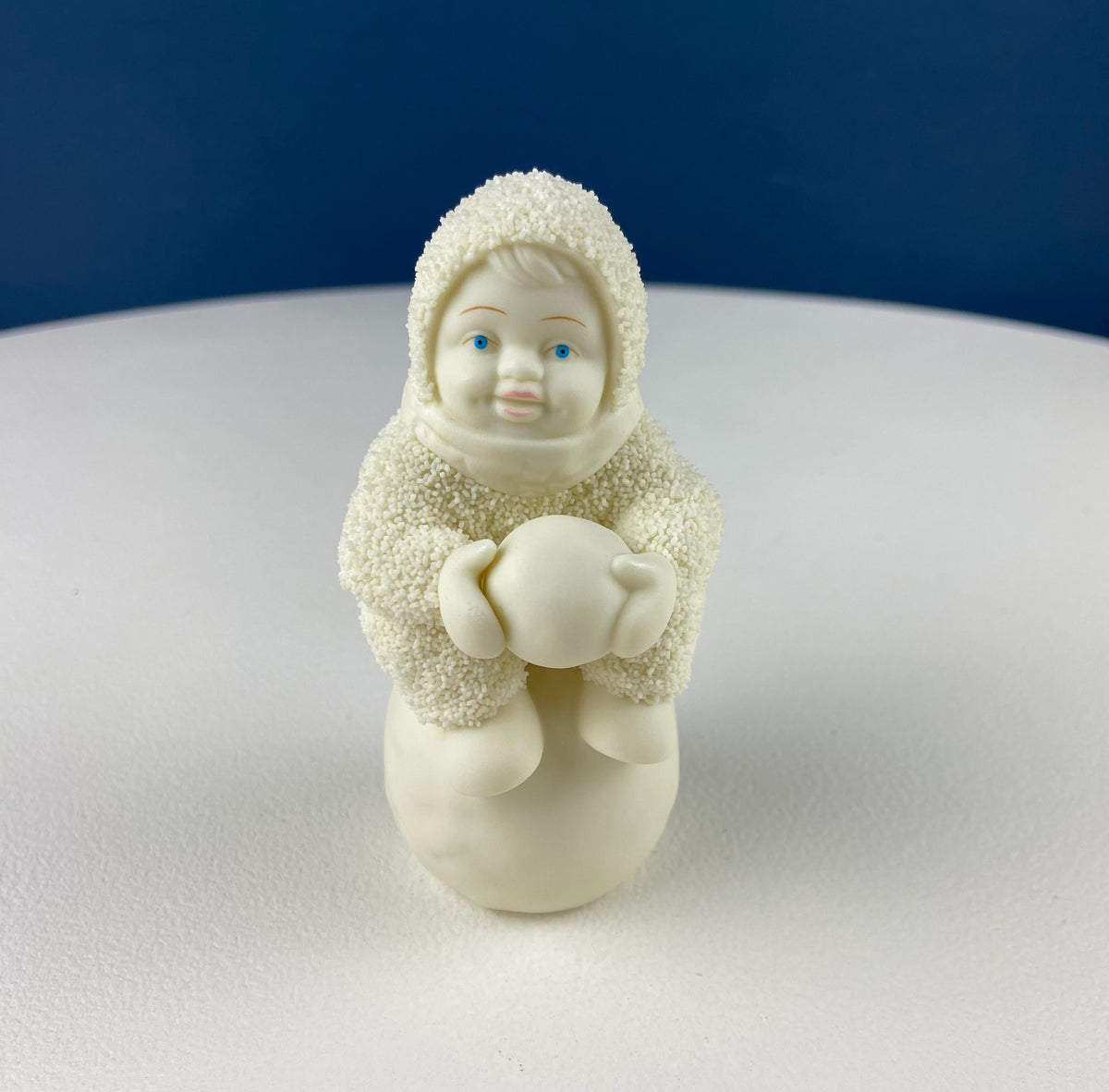 White porcelain snowbaby figurine in hood and scarf holding a heart ornament