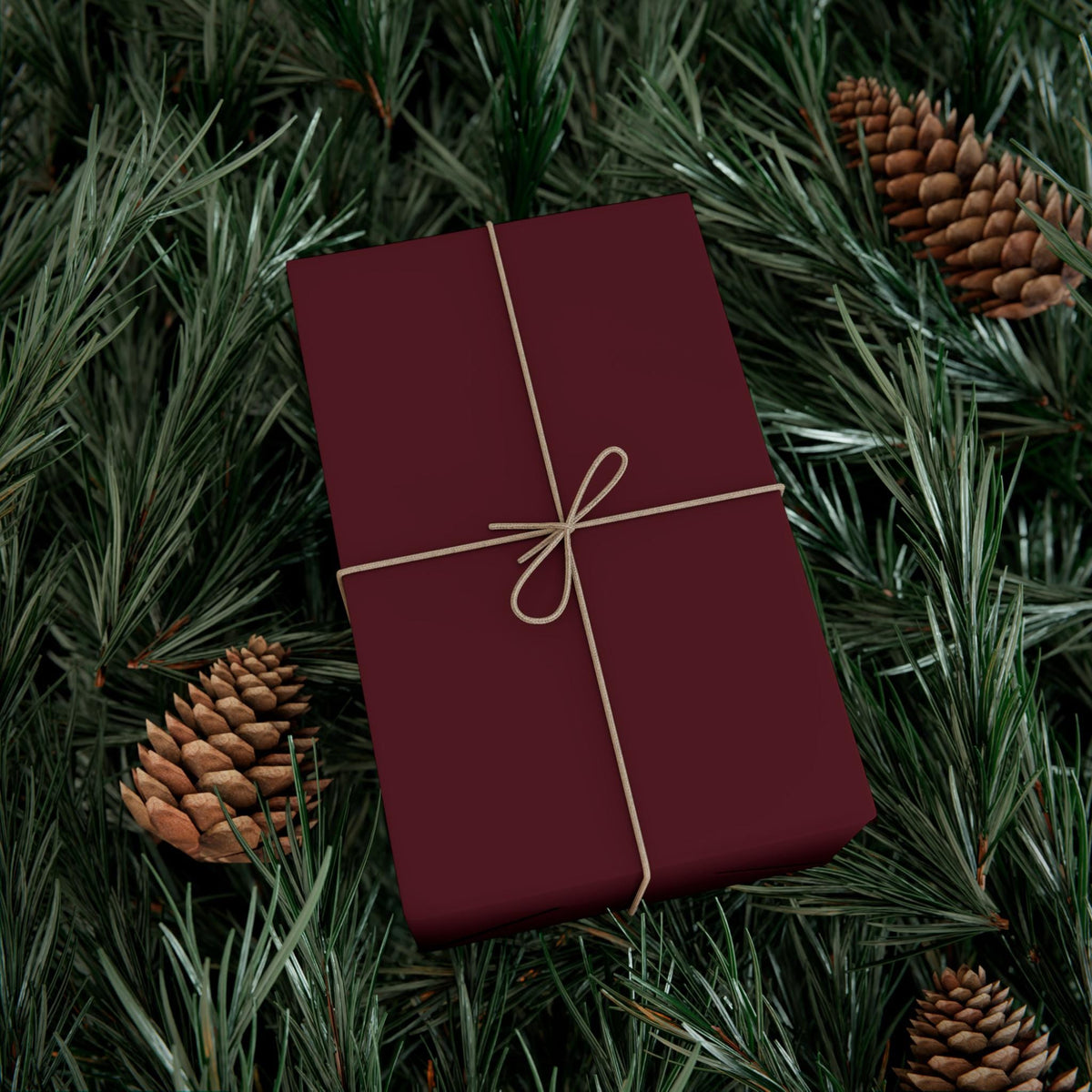 Burgundy gift-wrapping paper tied with a gold string bow on evergreen branches