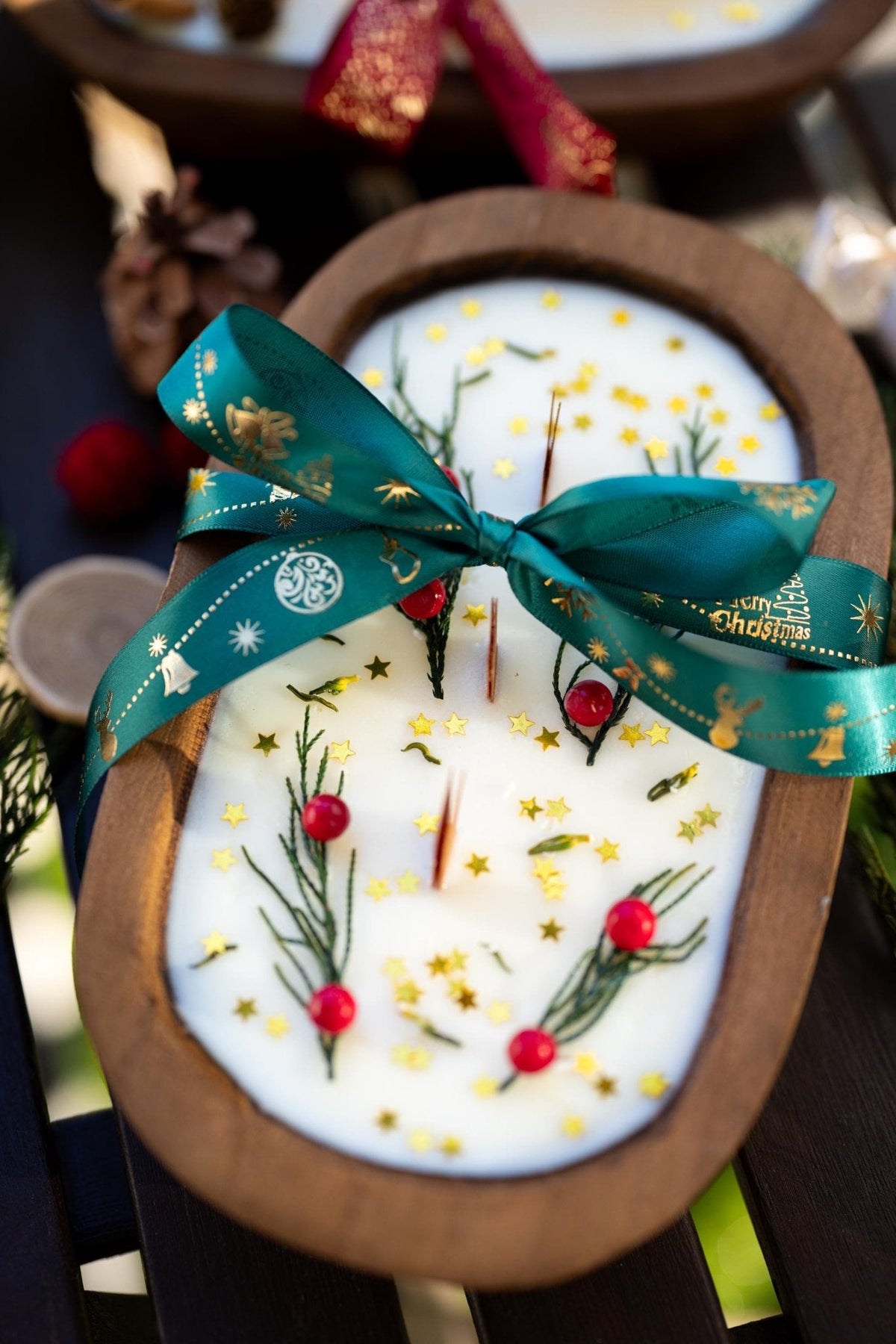 Wood dough bowl candle with white wax holiday sprigs and teal ribbon across the top