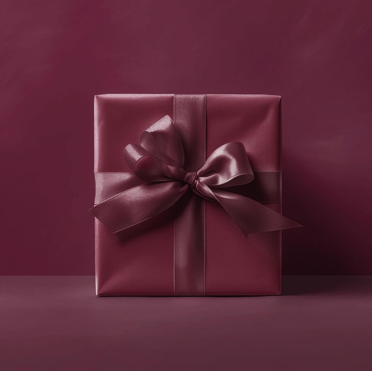 Burgundy gift box wrapped in solid wrapping paper with satin bow and ribbon