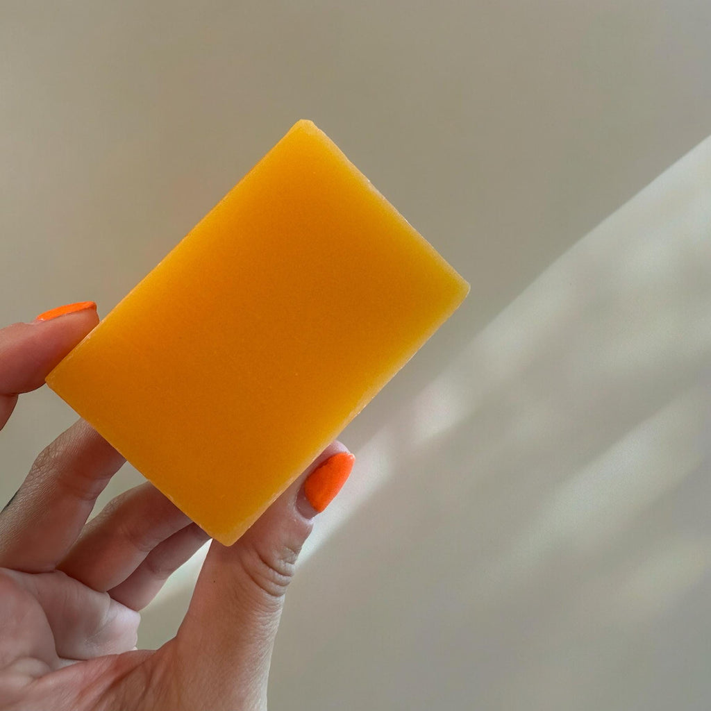 Orange-yellow square soap bar held in hand, smooth bar surface