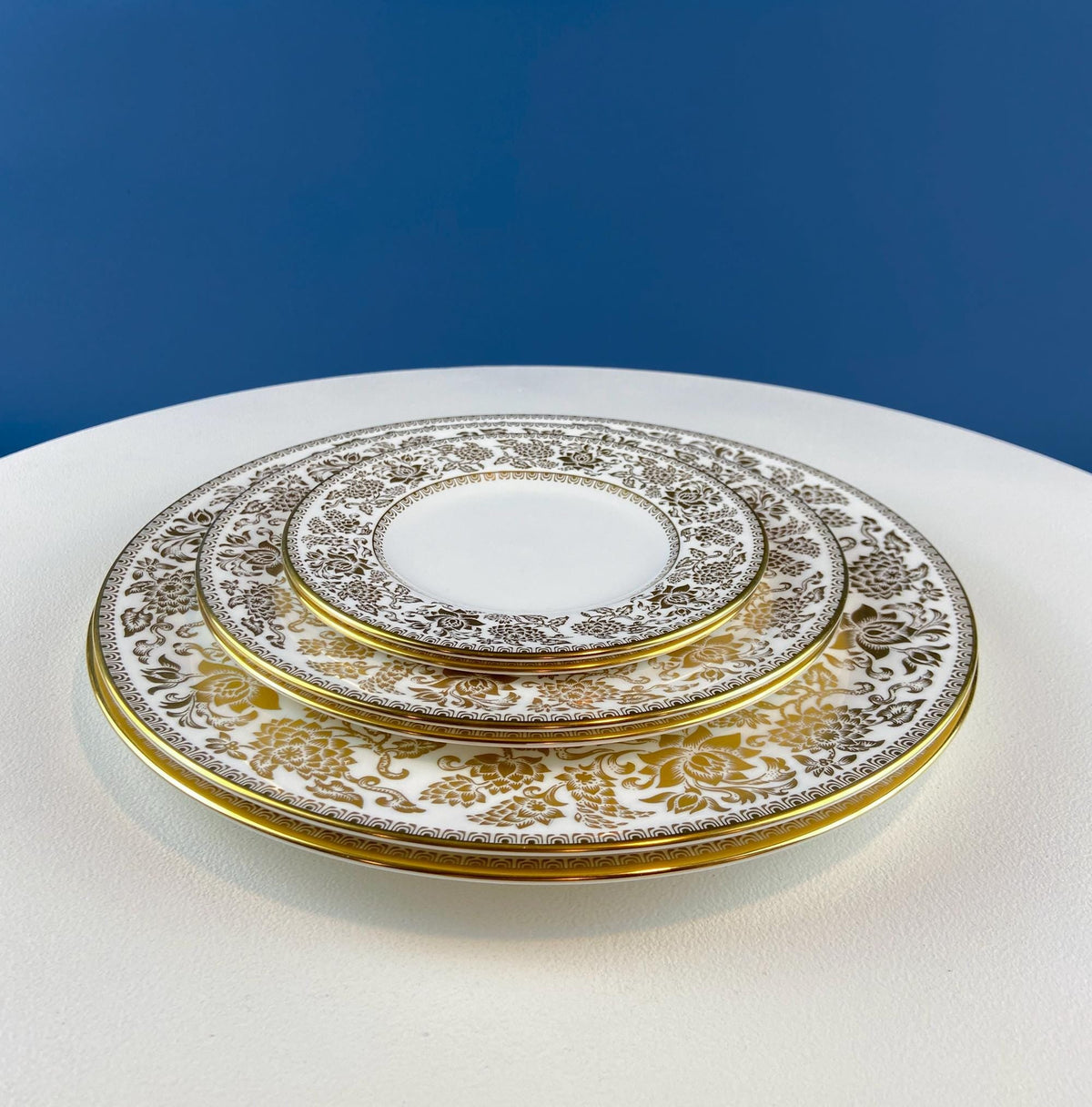 Stacked porcelain plates with intricate gold damask pattern and thin gold rim