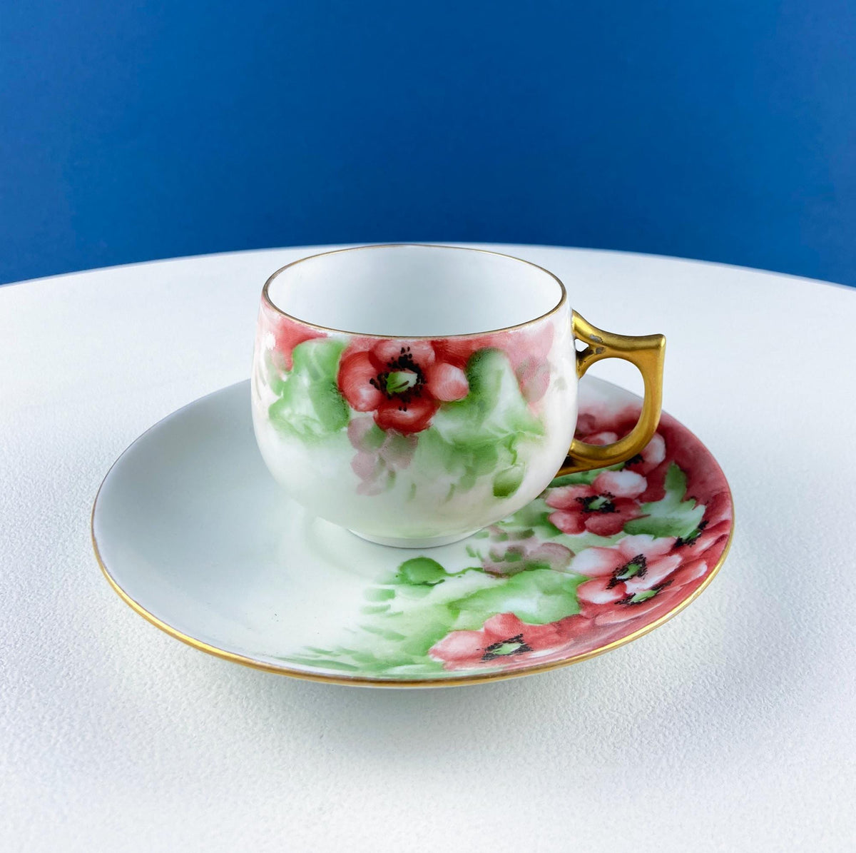 Porcelain tea cup and saucer with pink berries, green leaves, and gold handle