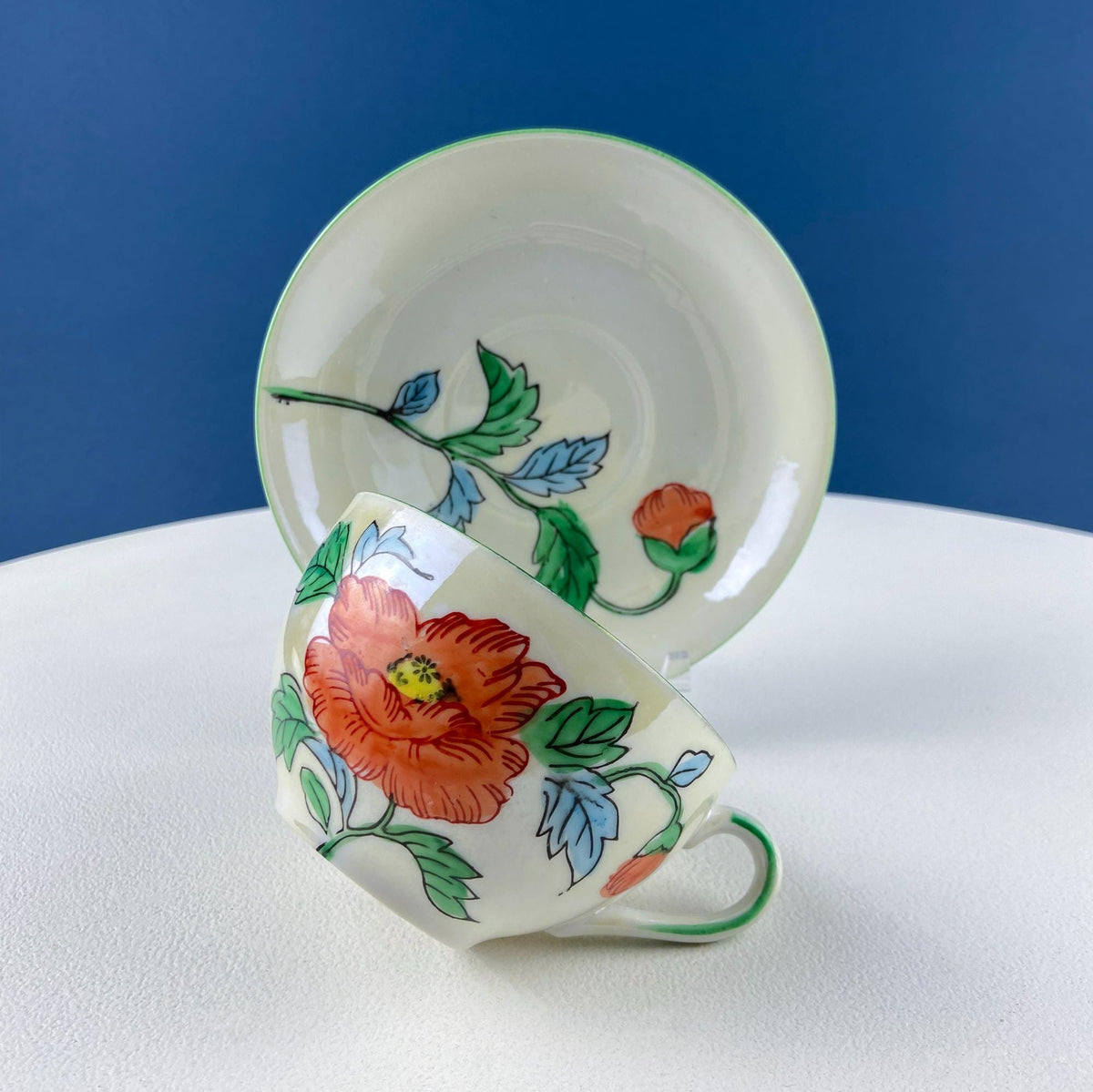 Porcelain tea cup with orange flowers and blue-green leaves, curved handle