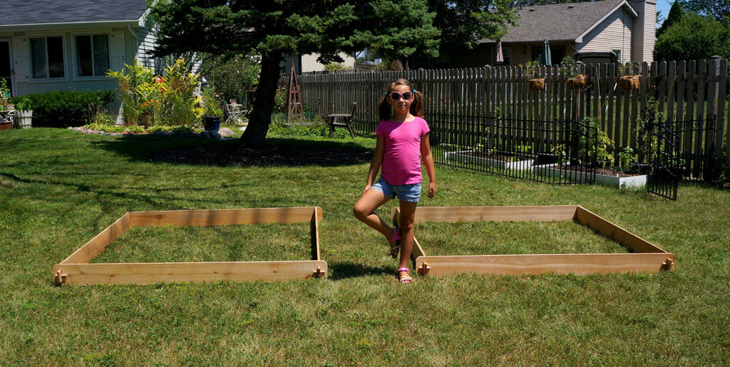 Two cedar raised garden beds with soil and young plants on a lawn