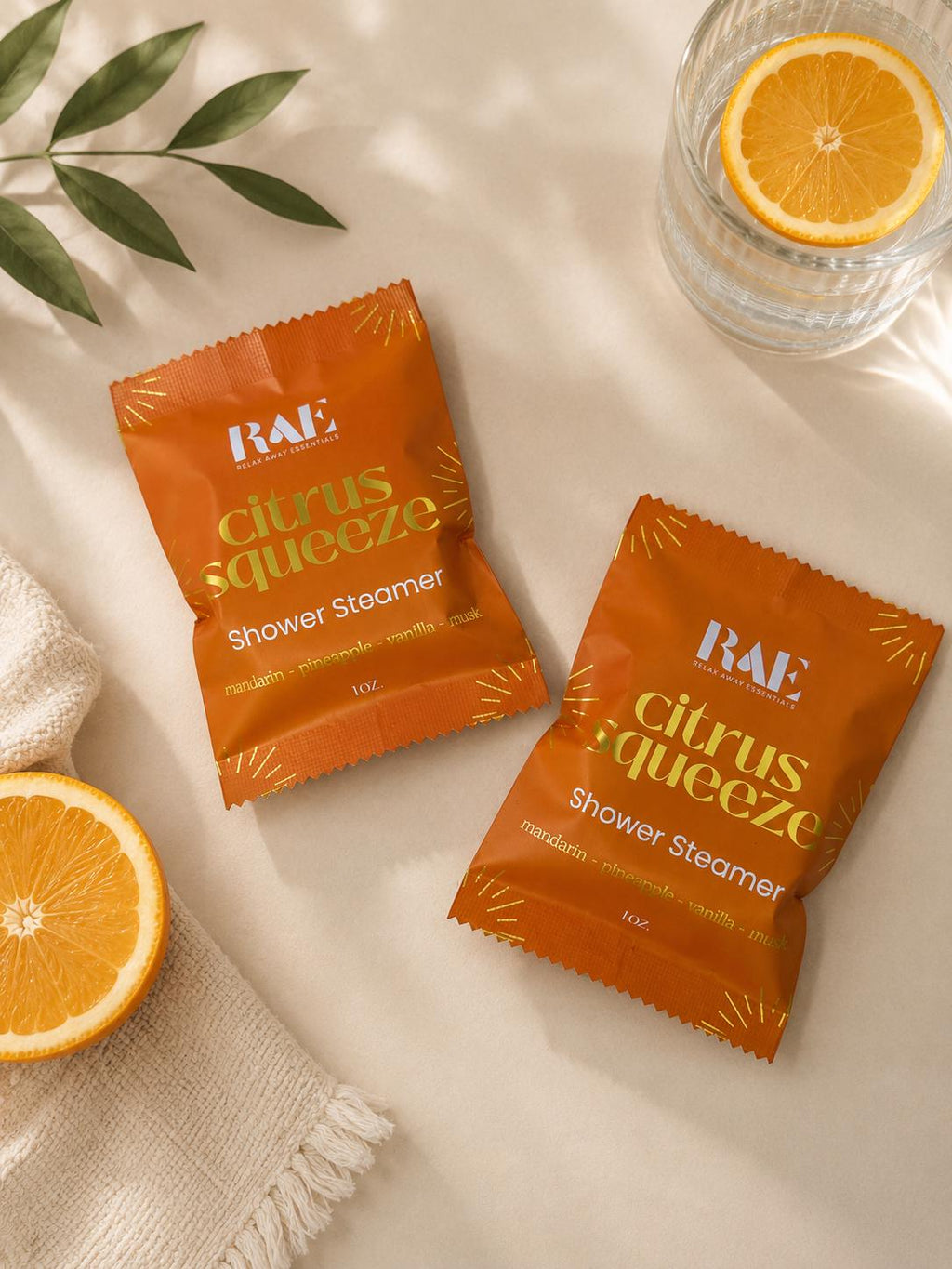Two RAE citrus squeeze shower steamer packets, orange with printed label