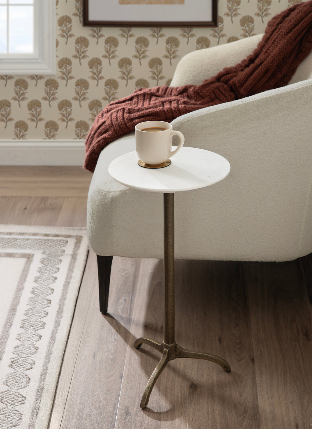 Round white marble side table holding a white mug on a bronze pedestal base
