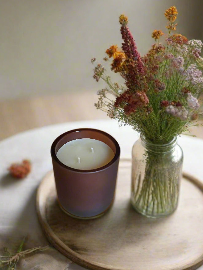 Unlit beeswax candle in dark brown glass jar with a flat wick centered.